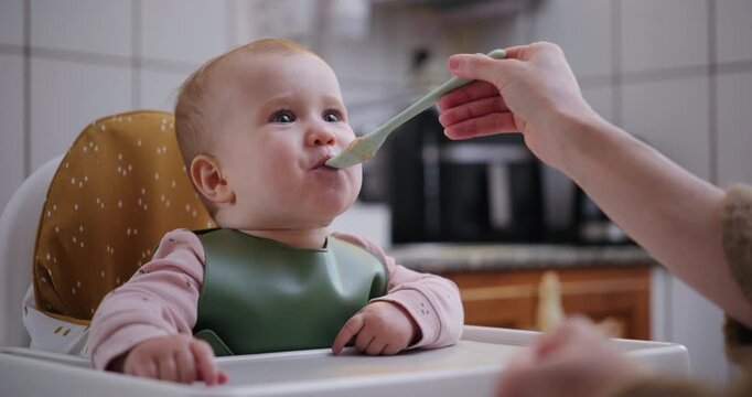Excited baby girl laughing and opening mouth for food from spoon