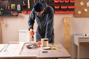concept of Craftsman and DIY handmade. man carpenter applies paint using paintbrush in carpentry...
