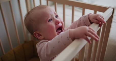 Sad baby girl crying and reaching out from wooden crib - Powered by Adobe