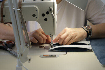 Skilled female seamstress using a sewing machine to create fabric items, showcasing craftsmanship and attention to detail in a bright, organized workspace with tools nearby