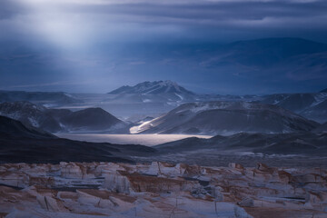 High-resolution shot of a desolate mountain landscape featuring dramatic light breaking through clouds over rugged terrain and unique geological formations.