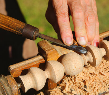 elderly artisan fingers processing wooden piece with lathe and chisel tool