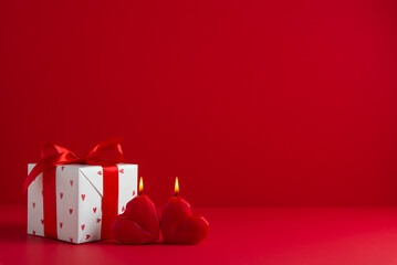 Gift, present box decorated with red ribbon bow and hearts, red heart shaped candles on red background. Valentine's day, 14 February, birthday, 8 march women's day gift. Love and romance.
