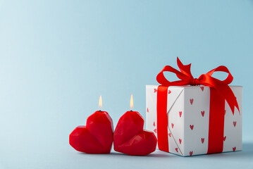Gift, present box decorated with red ribbon bow and hearts, red heart shaped candles on light blue background. Valentine's day, 14 February, birthday, 8 march women's day gift. Love and romance.