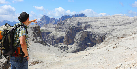 man hiker with backpack and hat pointing with his finger to top mountain he has to reach before evening © ChiccoDodiFC