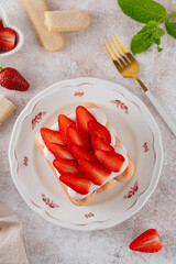 Strawberry tiramisu. Italian layered dessert with mascarpone cream and biscuits on a plate with cup of coffee on a concrete background.