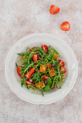 Healthy salad with strawberries, tomatoes, arugula, halloumi cheese and basil on a plate on a concrete background. Top view, copy space.