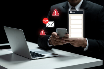 Businessman using a smartphone with a message notification and an email alert while working on a laptop. Concept of Scam