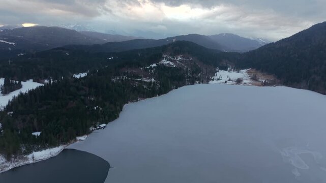 Winter drone view of Lake Barmsee in Bavaria, Germany. Aerial panorama shows icy lake surface, alpine nature and mountain landscape near Mittenwald. Luftbild des Barmsees in Oberbayern, Deutschland