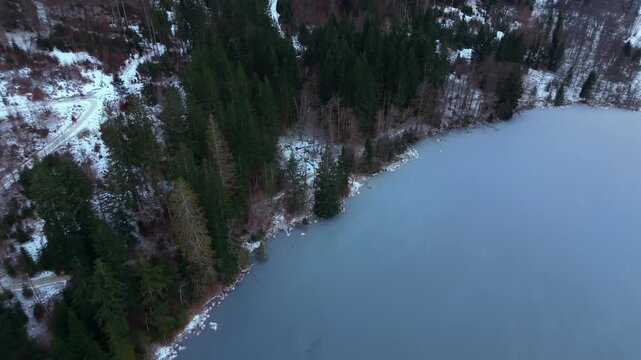 Hiking area near Kruen. Aerial view of snowy trails and lake. Drone footage above Barmsee north of Mittenwald, Germany. Winter aerial view of frozen lake surrounded by forest and alpine meadows.