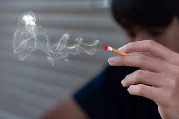 Closeup hand holding lighted cigarrette smoking of asian young adult who starting to smoke in private area of house to avoid punishment from his family, relatives or parents.