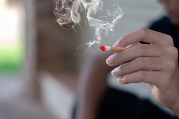 Closeup hand holding lighted cigarrette smoking of asian young adult who starting to smoke in private area of house to avoid punishment from his family, relatives or parents.