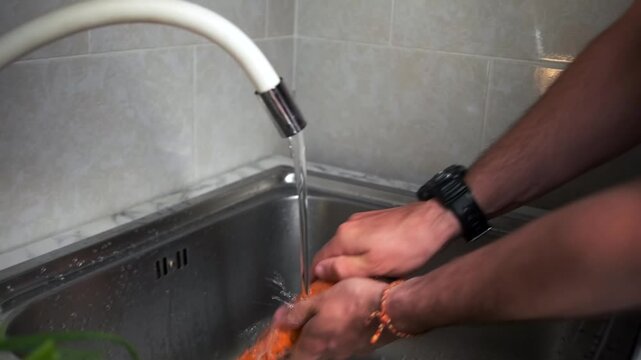 Before cooking male hands wash a large carrot under water jet in a kit