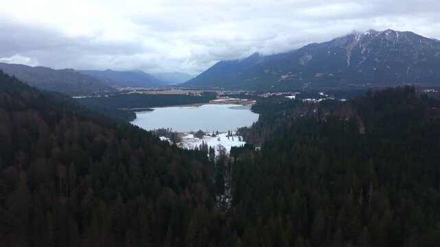 Aerial drone video of Lake Barmsee in Bavaria, Germany. Winter landscape with a partially frozen alpine lake near Kruen north of Mittenwald, surrounded by forest, meadows and Karwendel mountains