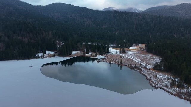 Drone video of Barmsee lake in Oberbayern, Germany. Winter aerial scenery with light snow, ice and Karwendel mountain range. Scenic winter nature from above in the Bavarian Alps region.