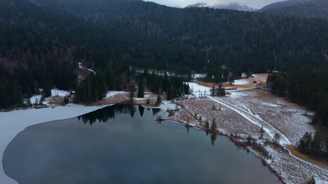 Drone shot over Lake Barmsee in the Bavarian Alps. Winter aerial panorama with icy water, forest and calm mountain scenery. Stunning aerial view of the Drei-Seen-Wanderweg area in snow.