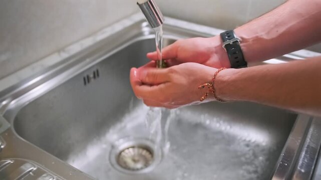 Male hands with a watch carefully wash ripe red strawberries under col
