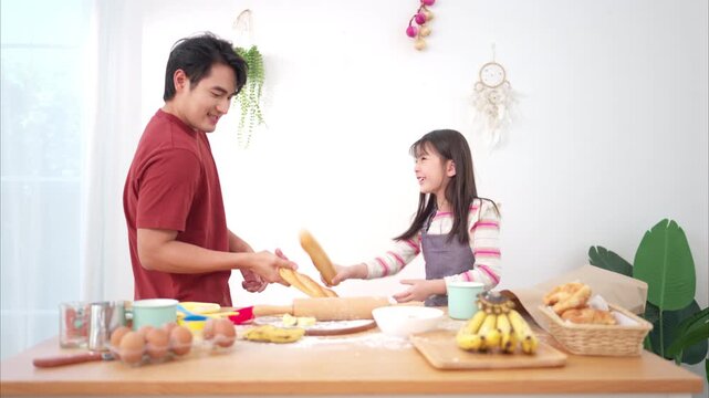 A father and daughter playfully sword-fight with baguettes in the kitchen, creating a fun and lively family cooking moment