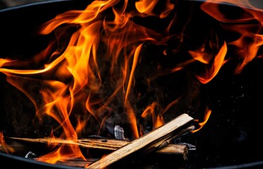 Fire flames and heat rise from burning wood in a campfire or bonfire set in a fire pit, with smoke and sparks in the dark. Use it for outdoor safety, survival, and camping content.