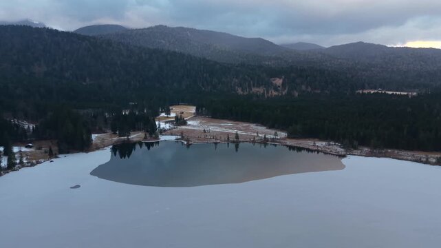 High angle view of snow-covered forests surrounding Lake Barmsee. Aerial footage of Barmsee near Kruen, Bavaria. Winter drone view of a peaceful alpine lake with frozen water and surrounding forest.