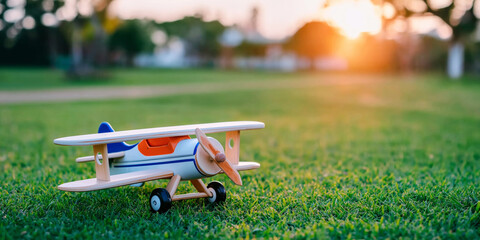 Wooden toy airplane sitting on green grass, golden hour sun light, symbolizing childhood dreams and imagination