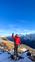 Obraz premium Adventurous man in a vibrant red jacket stands triumphantly atop snowy peaks, embracing mountain serenity and Winter Solstice spirit