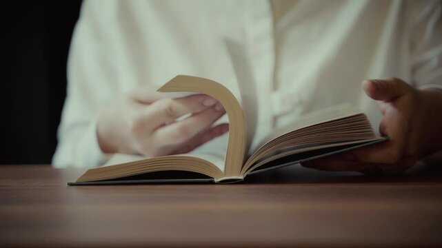 Close-up of hands turning pages of an open book on a wooden table