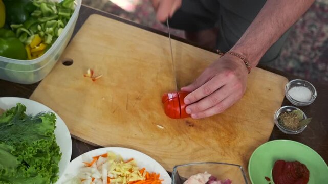 Male hands slice a ripe red tomato on a wooden cutting board. Nearby b