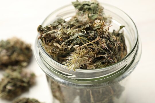 Dried medicinal herbs in jar on white table, closeup