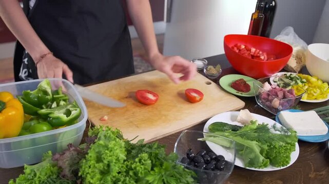 In the kitchen a woman cuts the stem base from half of a ripe red toma
