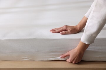 Woman putting bed sheet on mattress indoors, closeup. Space for text