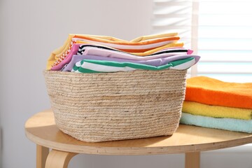 Laundry basket with clothes and towels on wooden table indoors, closeup