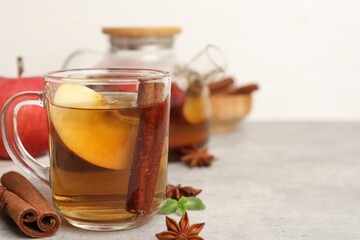 Aromatic fruit tea in glass cup, teapot, apple, mint and spices on grey table, closeup. Space for text