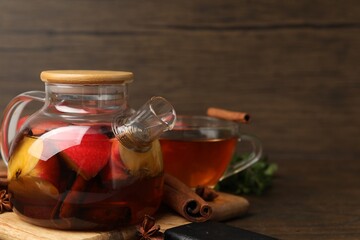 Aromatic fruit tea in glass teapot, cup, mint and spices on wooden table, closeup. Space for text