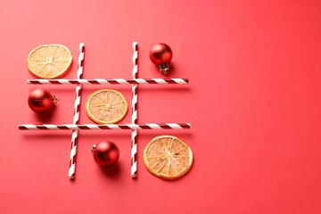 Tic tac toe game made with baubles and dry orange slices on red background. Space for text