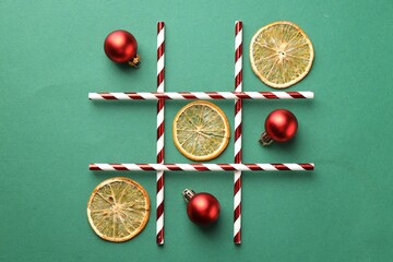 Tic tac toe game made with baubles and dry orange slices on green background, flat lay