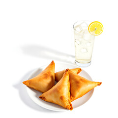 A plate of samosas and a refreshing glass of lemonade on a white background