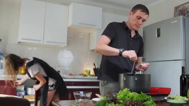 The man adds a pinch of salt to a pot where spaghetti cooks in thick t