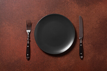vintage knife fork and black plate on brown background