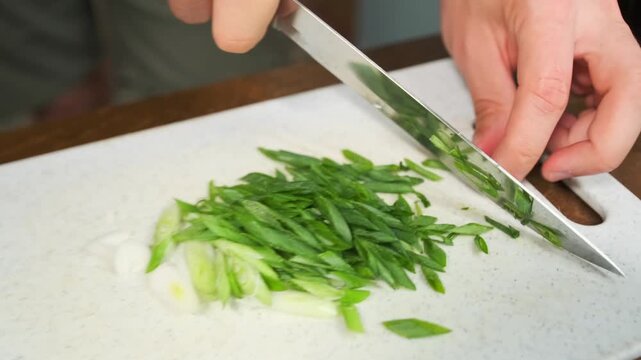 Male hands use a sharp knife to slice fresh crisp aromatic green onion