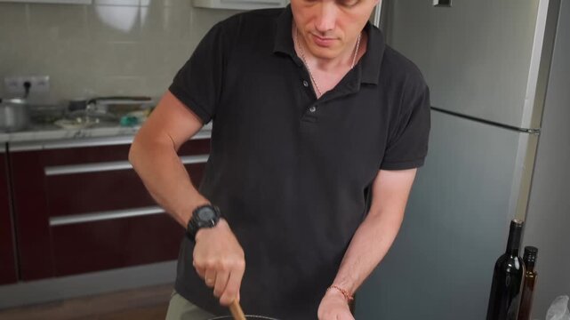 A man stirs vegetable stew in a pot with a wooden spatula. In the thic