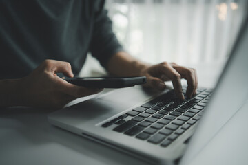 Hands using smartphone while typing on laptop keyboard, showcasing multitasking, digital marketing, remote office work, content creator, checking work, seo trends and modern business communication