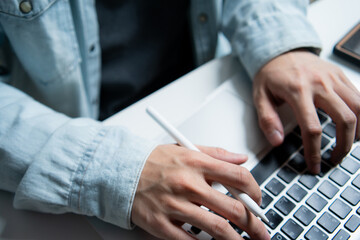 Hands typing on laptop keyboard while holding a pen, representing multitasking, digital design, remote work, content creator, seo marketing, copywriting and modern creative business workflow