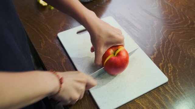 Female hands cut a fresh crisp sweet-sour apple on a white cutting boa
