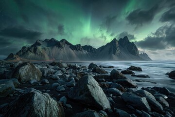 Jagged mountain range under a glowing aurora borealis, foreground rocks and sea