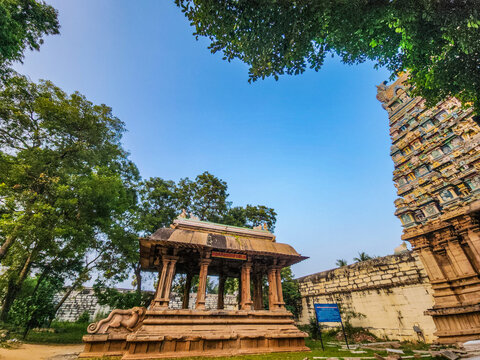 Ancient South Indian temple with stone mandapam and ornate gopuram framed by greenery in Thiruvathavur, Madurai, Tamil Nadu