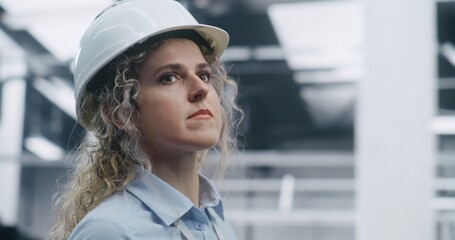 Close Up Female Technical Specialist Wearing Shirt and ID Badge, Overseeing Robotic Assembly Process in Clean, Modern Plant in Safety Helmet. Concept of Safety Protocols in Advanced Automation.