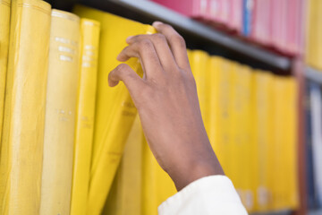 Close up of hand search for book on bookshelves in library. Hand reaching a book on library shelf. Library and book on shelf