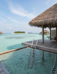 Fototapeta premium Idyllic beachfront resort with thatched roof structures and crystal clear turquoise water paradise