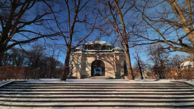 Historischer Hubertusbrunnen am Ostende des Nymphenburger Kanals in Muenchen, Deutschland. Klassizistisches Baudenkmal im Schnee an einem sonnigen Wintertag in Neuhausen-Nymphenburg, Bayern.
